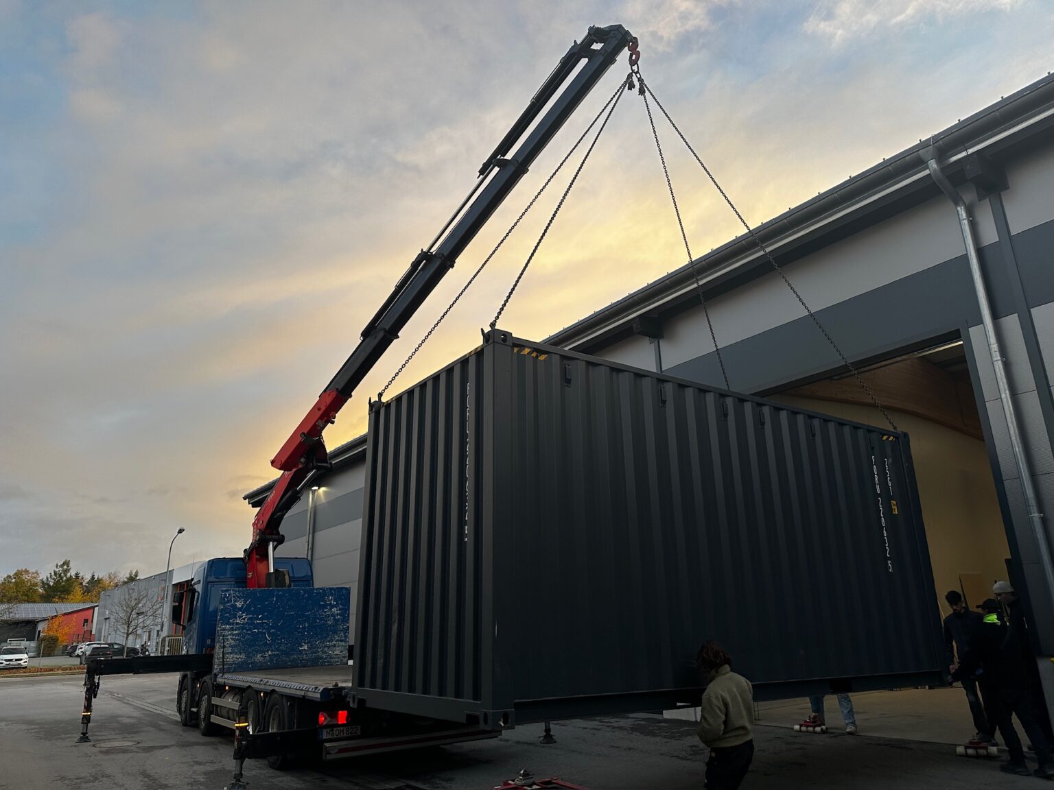 Container wird in der Abenddämmerung per Kran vom LKW gehoben