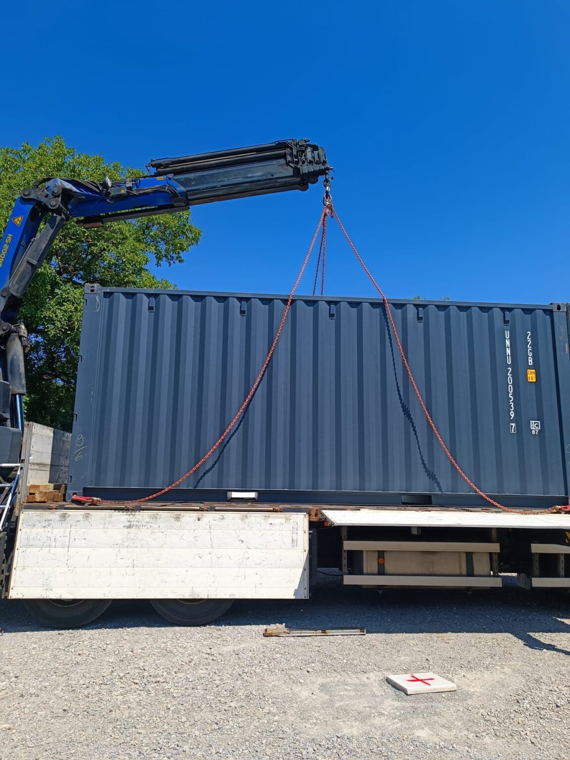 Anthrazitfarbener 20-Fuß-Container hängt an den Ketten des Ladekrans über der Pritsche