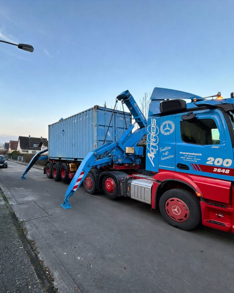Lastwagen mit blauem Ladekran liefert einen gebrauchten 20-Fuß-Container in einer Wohnstraße an
