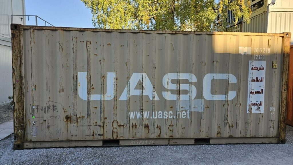 Gebrauchter 20-Fuß-Container in Beige mit Rostspuren und UASC-Aufschrift, Seitenansicht im Depot