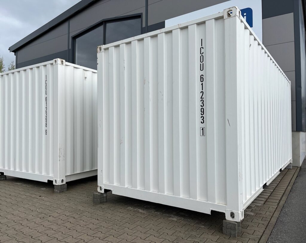 Zwei weiße 20-Fuß-Container nebeneinander auf Stahlplatten vor einer Gewerbehalle