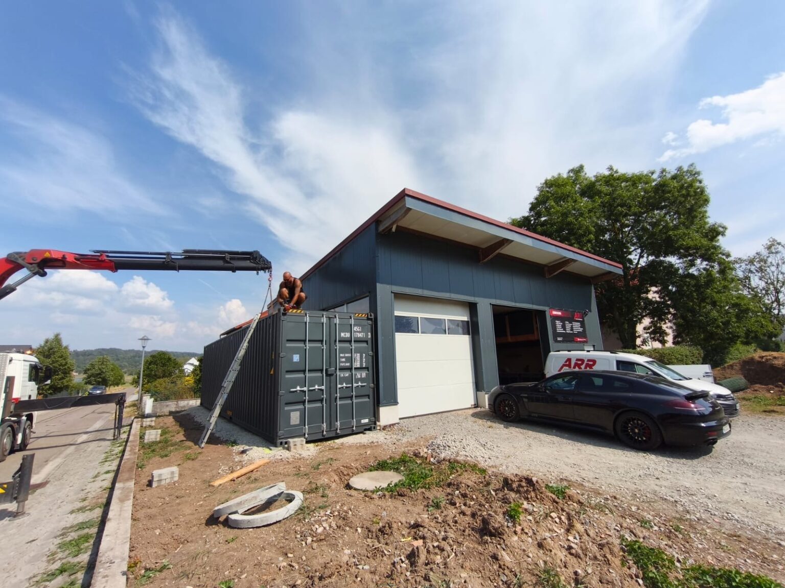 Dunkler 40-Fuß-Container wird per Ladekran neben einer neuen Halle abgesetzt
