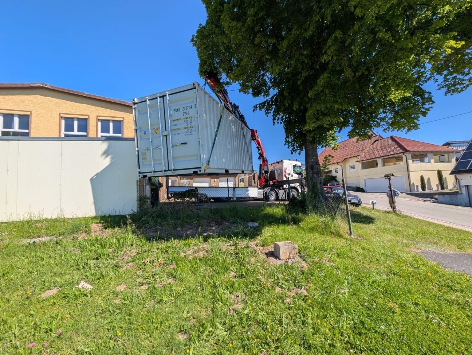 Weißer 20-Fuß-Container schwebt am Ladekran über einer Grundstücksecke