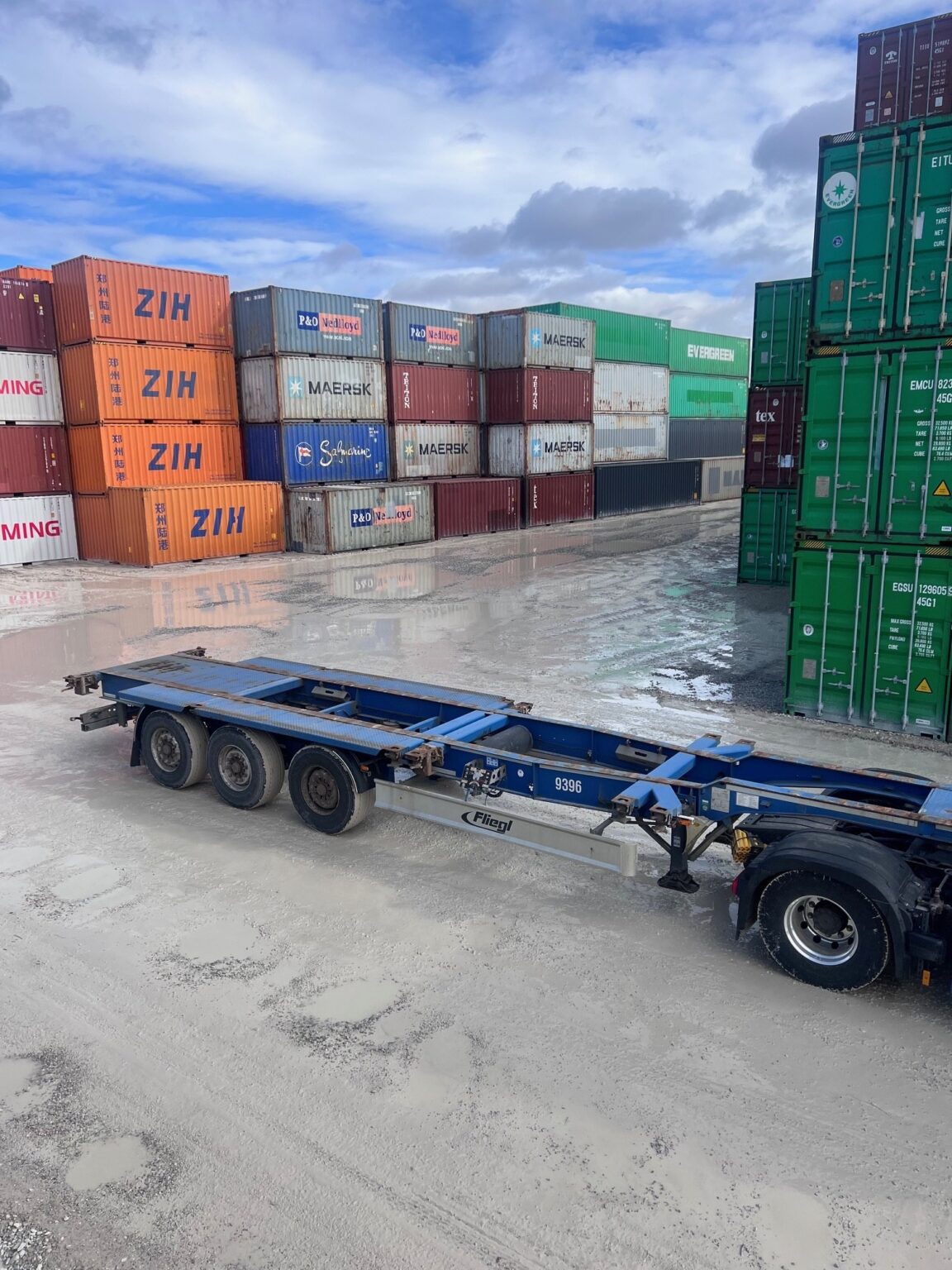 Gestapelte Seecontainer im Depot, davor ein leerer Containerauflieger