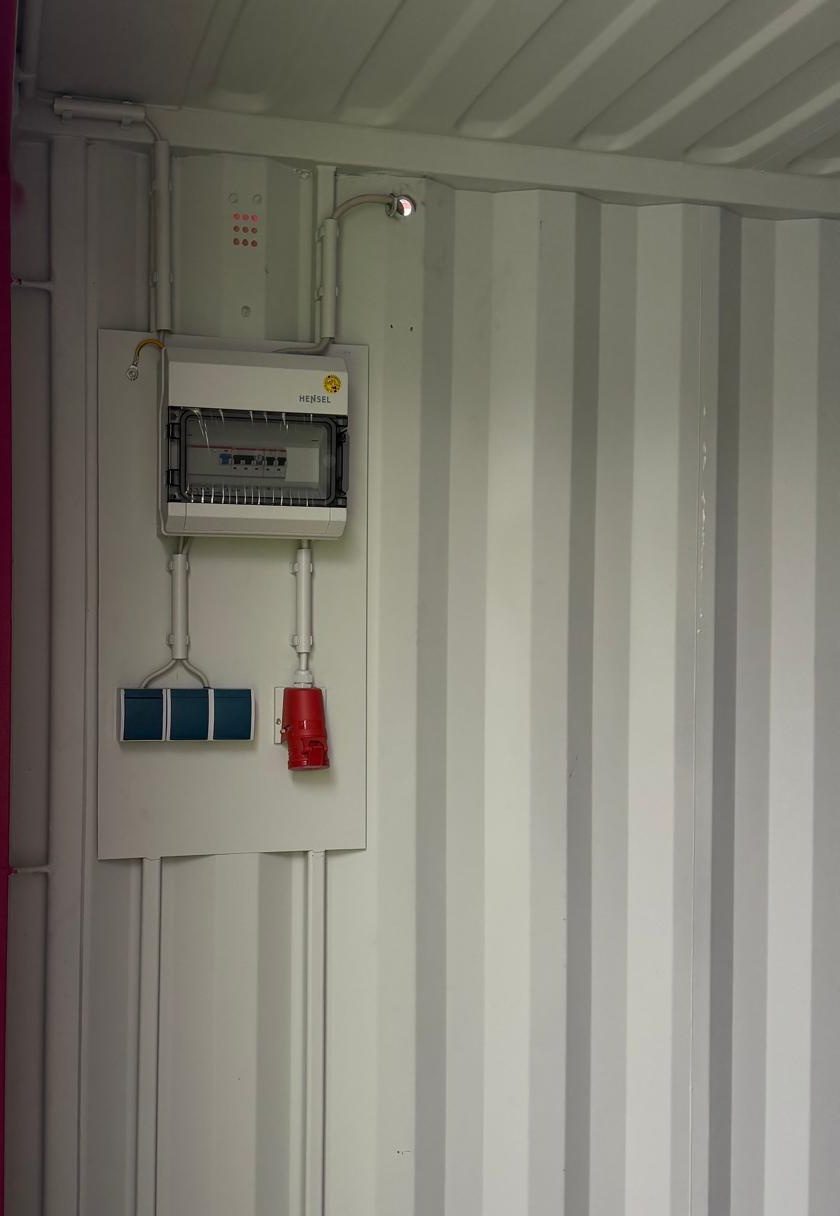 Elektroinstallation in einem 20-Fuß-Container: Kleinverteiler mit FI-Schutzschalter, Dreifach-Steckdosenblock und rotem CEE-Anschluss auf einer Montageplatte