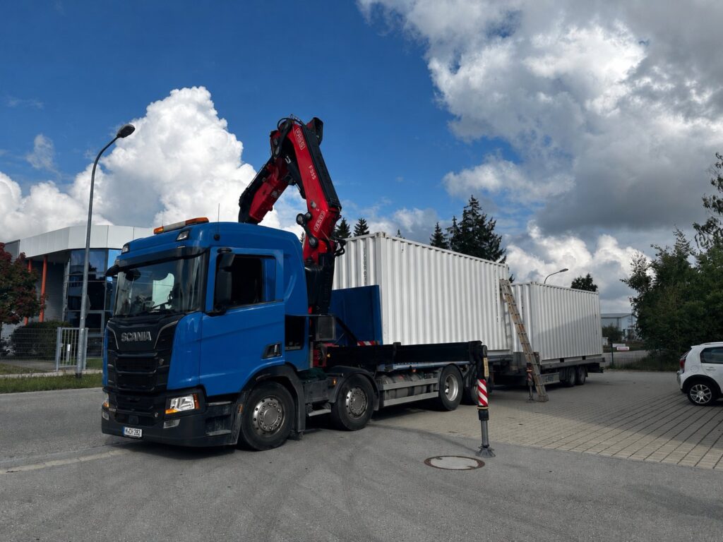 Blauer Lastwagen mit rotem Ladekran, dahinter zwei weiße Container auf dem Anhänger