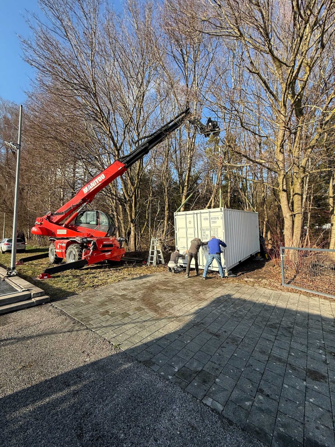 Roter Teleskoplader setzt einen weißen 20-Fuß-Container auf dem Grundstück ab